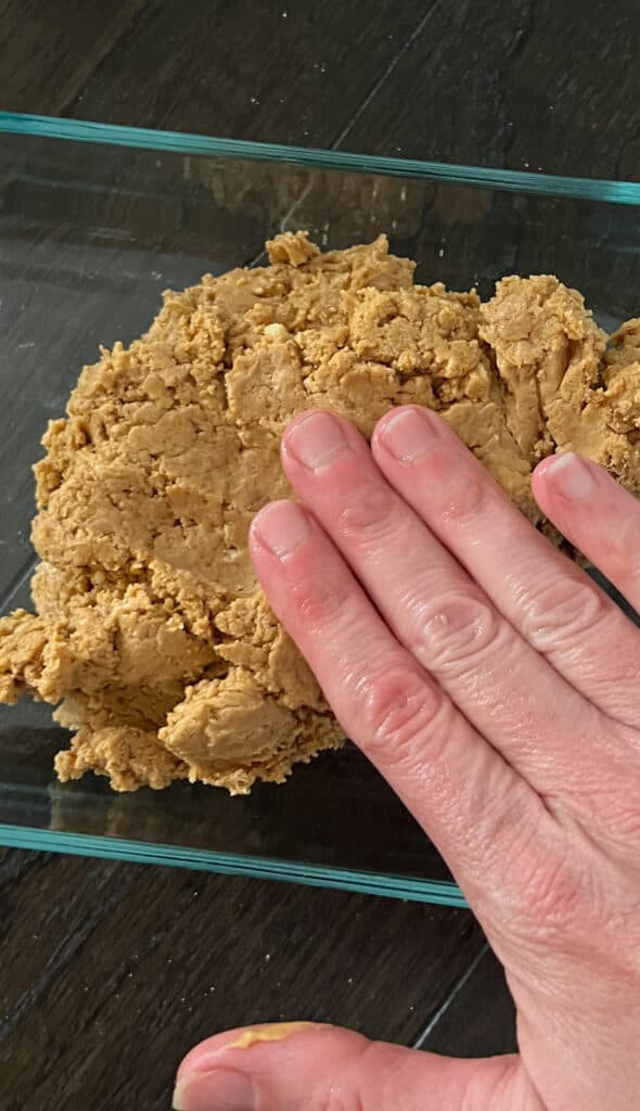 pictured are four fingers pressing peanut butter protein powder mixture into a pan.