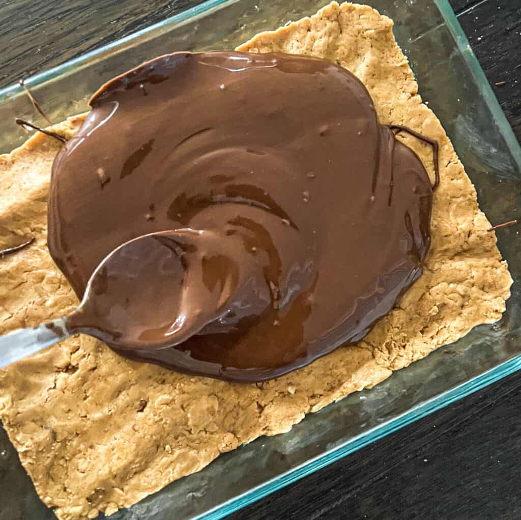 a picture of a spoon smoothing melted chocolate evenly over peanut butter protein bars. 