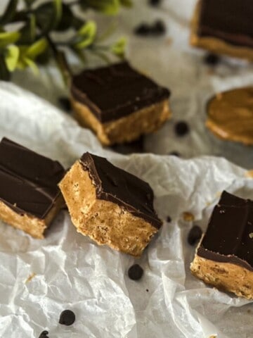 A close-up of a plate of peanut butter protein powder bars. The bars are golden brown in color and have a slightly textured surface. The bars are topped with chocolate chips.