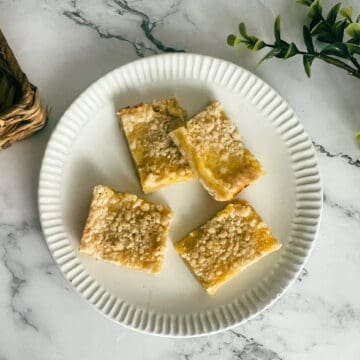 Image of luscious lemon bars on a plate. The bars have a golden crust topped with a creamy lemon filling. A light dusting of powdered sugar adds a touch of sweetness. These lemon bars are beautifully simple, showcasing the perfect balance of flavors in just five ingredients or less.