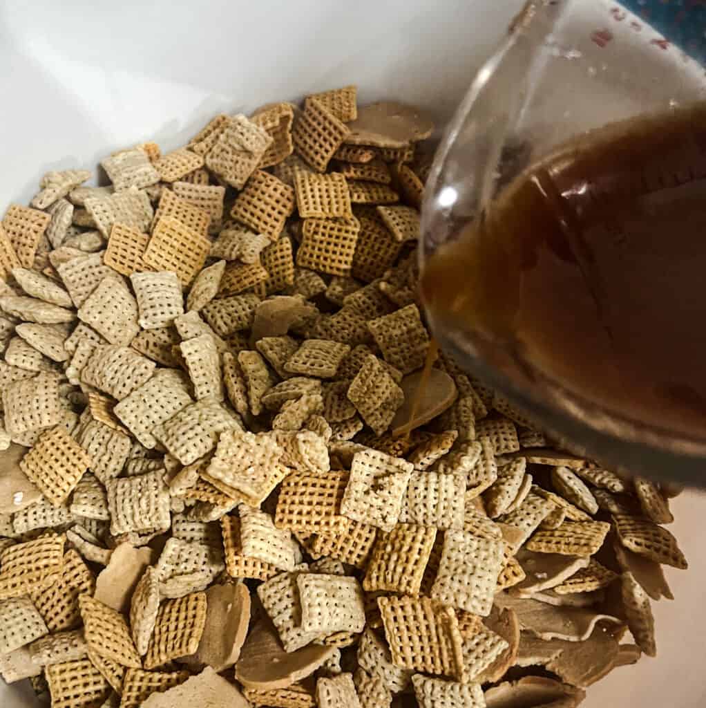 pouring seasoning mixture over homemade chex mix. The butter mixture is made up of melted butter, worcestershire sauce, onion powder, garlic powder and seasoning salt. 