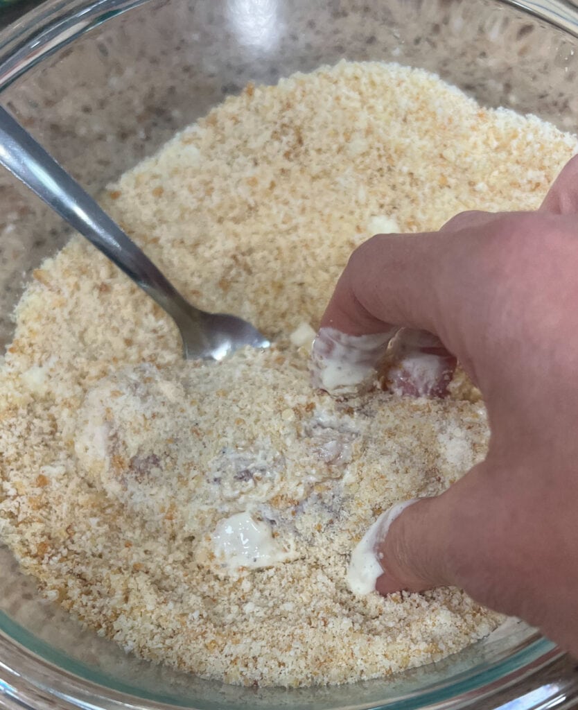 a person dipping chicken in crushed croutons and parmesan cheese. 