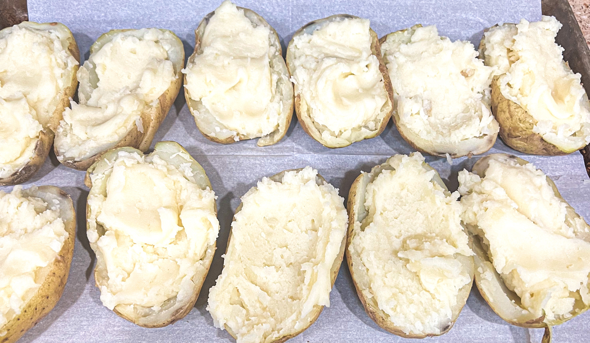 a picture of twice baked potatoes with the insides scooped out and mashed potatoes being placed inside to fill. 