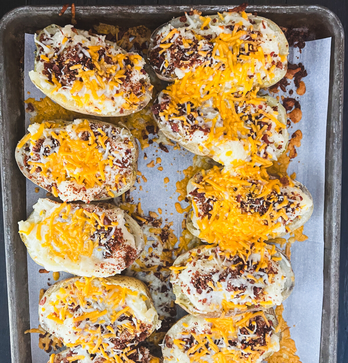 A twice baked potato with a cheesy, creamy filling and a crispy skin. The potato is halved and topped with cheese and bacon. 