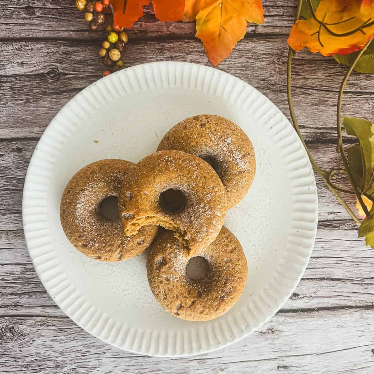 a pumpkin spice donut sitting on a white plate. The donut is round and has a hole in the center. It is topped with pumpkin spice and sugar. 