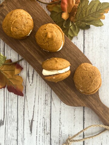 A close-up photo of a five-ingredient pumpkin whoopie pie. The whoopie pie is made with two soft and chewy pumpkin cookies sandwiched together with a creamy filling. The cookies are topped with a sprinkle of pumpkin pie spice