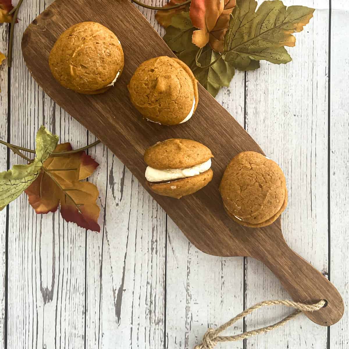  A close-up photo of a five-ingredient pumpkin whoopie pie. The whoopie pie is made with two soft and chewy pumpkin cookies sandwiched together with a creamy filling. The cookies are topped with a sprinkle of pumpkin pie spice