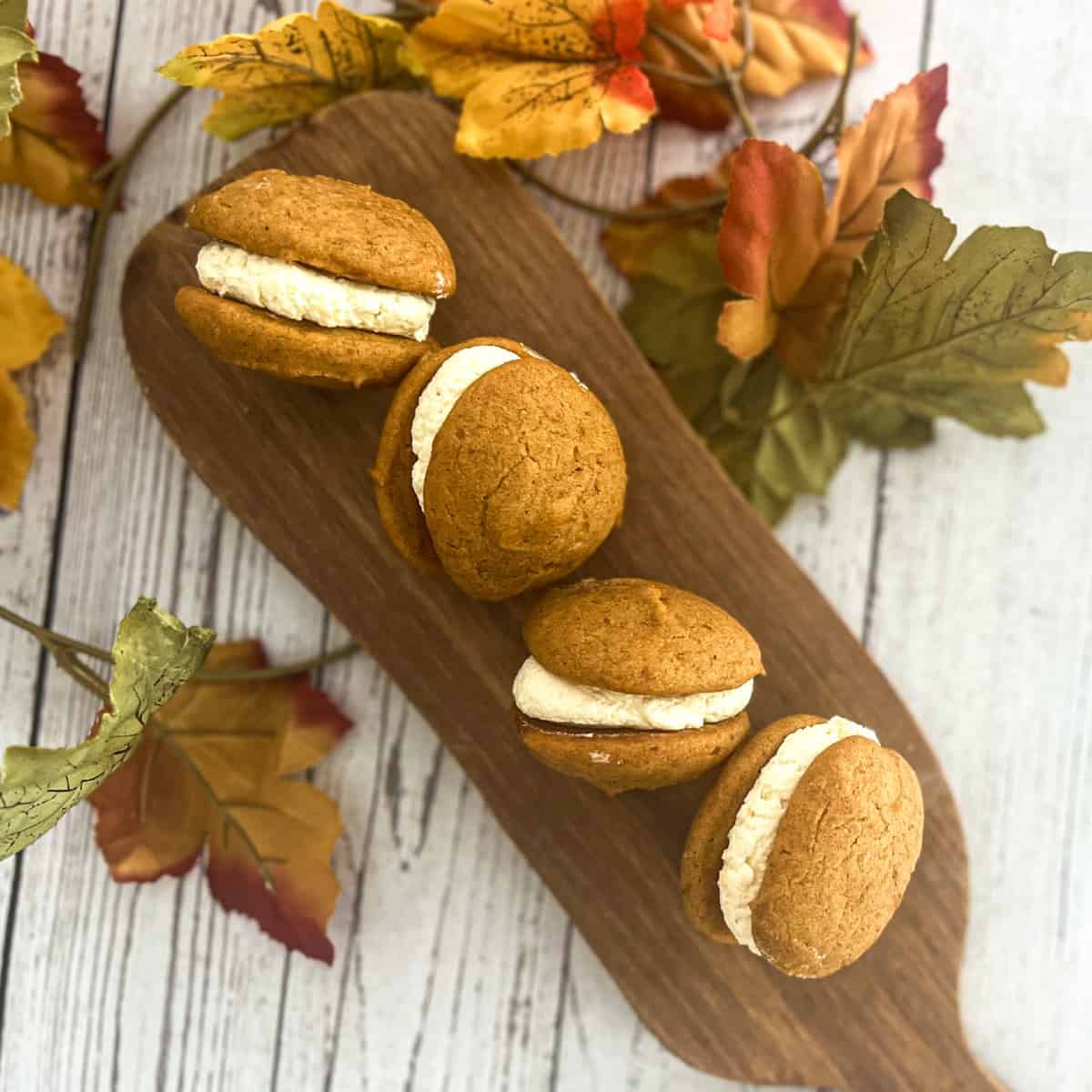 a close up picture of five ingredient pumpkin whoopie pie cookies. the soft poofy pumpkin cookies are filled with a cream cheese, cheesecake pudding or vanilla filling. 