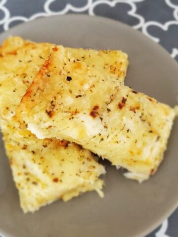 A close-up of a plate of Little Caesars Italian copycat cheesy bread recipe. The bread is golden brown and covered in melted cheese and garlic butter.