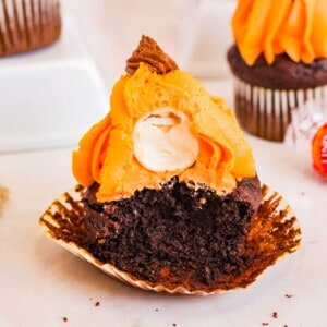 A close-up photo of four pumpkin cupcakes on a white plate. The cupcakes are topped with a generous swirl of cream cheese frosting. The frosting is smooth and creamy, and the cupcakes are moist and fluffy. The cupcakes are decorated with a sprinkle of pumpkin pie spice and a couple of chocolate chips.