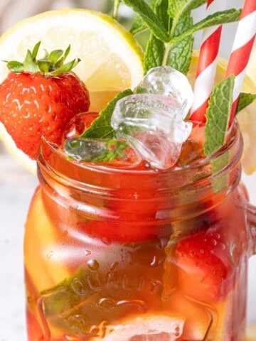 A tall glass brimming with a refreshing strawberry mojito mocktail, featuring muddled mint leaves, sliced strawberries, and a lime wedge, all topped with sparkling lime soda