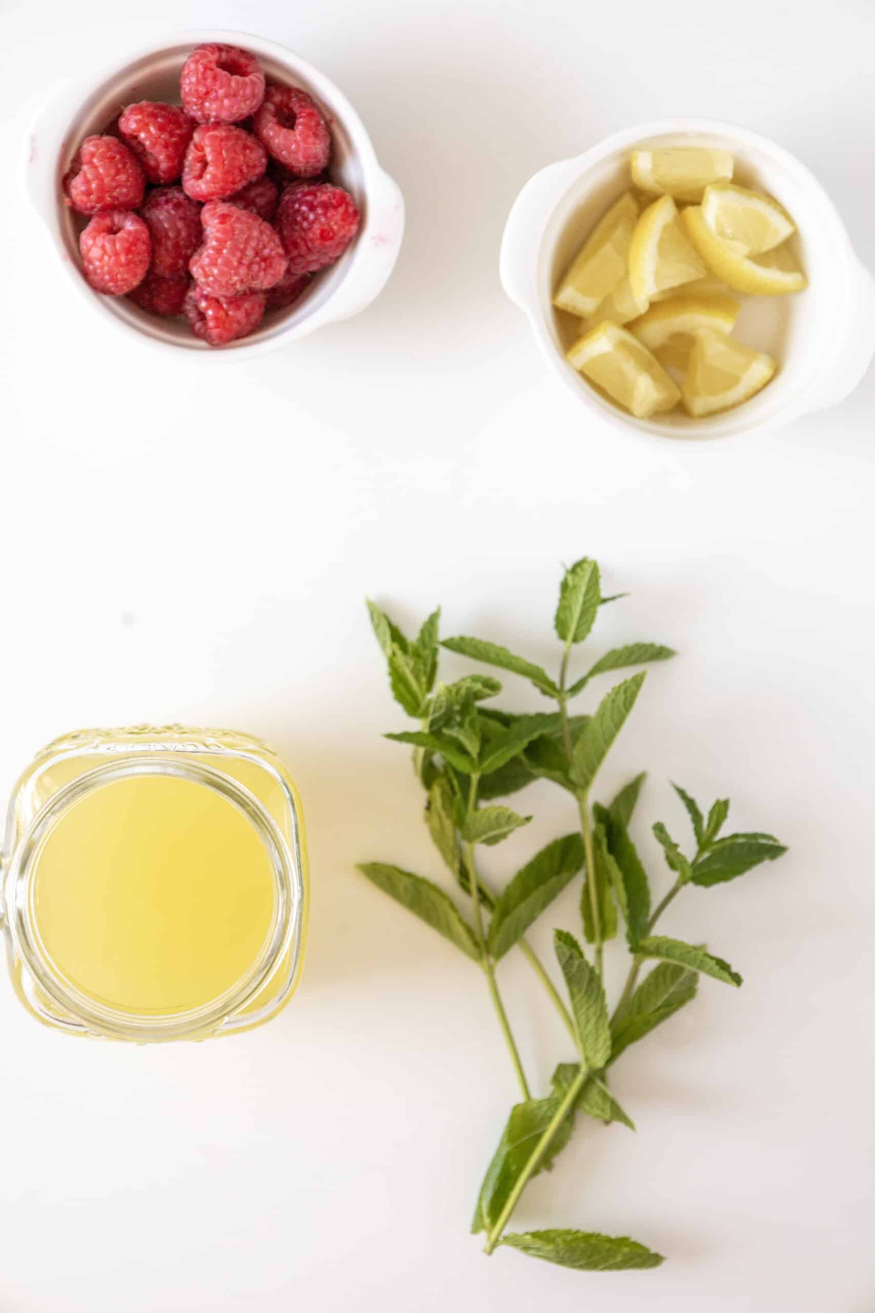 ingredients for raspberry mojito including raspberries, lemons, lemonade and mint