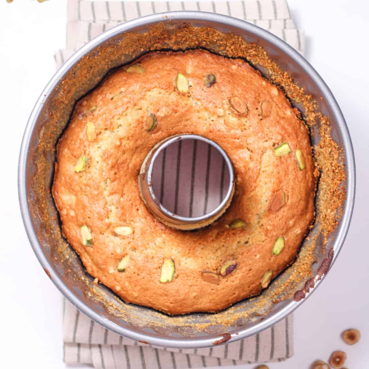 a photo of a pistachio pudding cake in a bundt pan. the bundt pan is sitting on a blue and white napkin