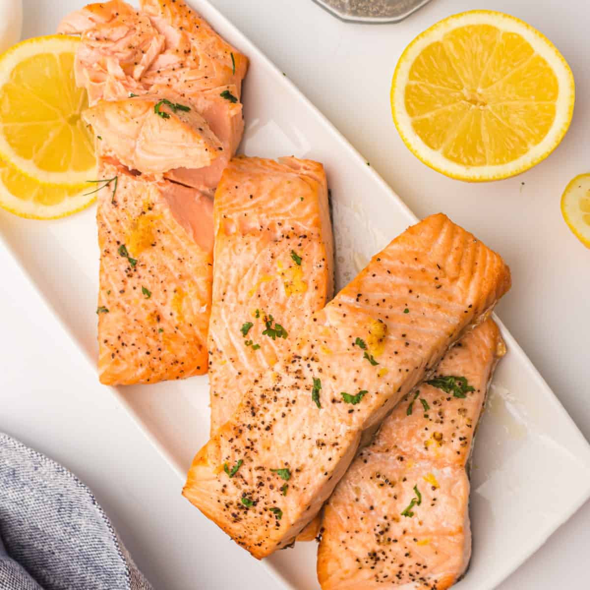 A flaky, cooked salmon fillet, air-fried from frozen, on a white plate with lemon slices.