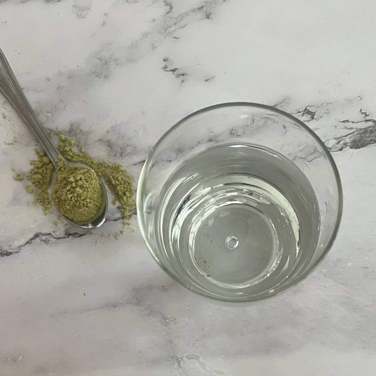 a cup filled with water with green matcha latte powder next to it on a spoon. 