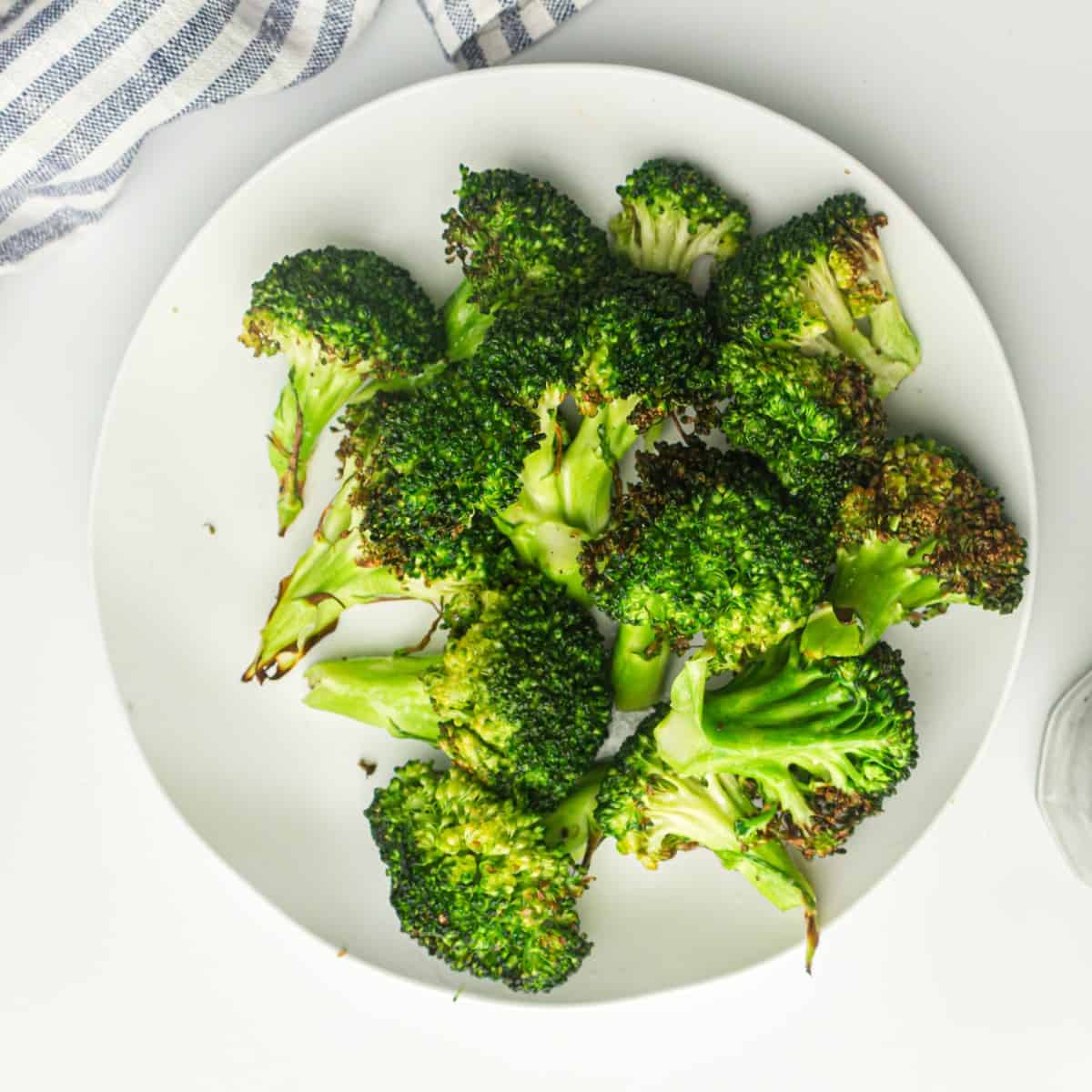 A white plate heaped with air fryer frozen broccoli florets. The broccoli is green with slightly crispy tips