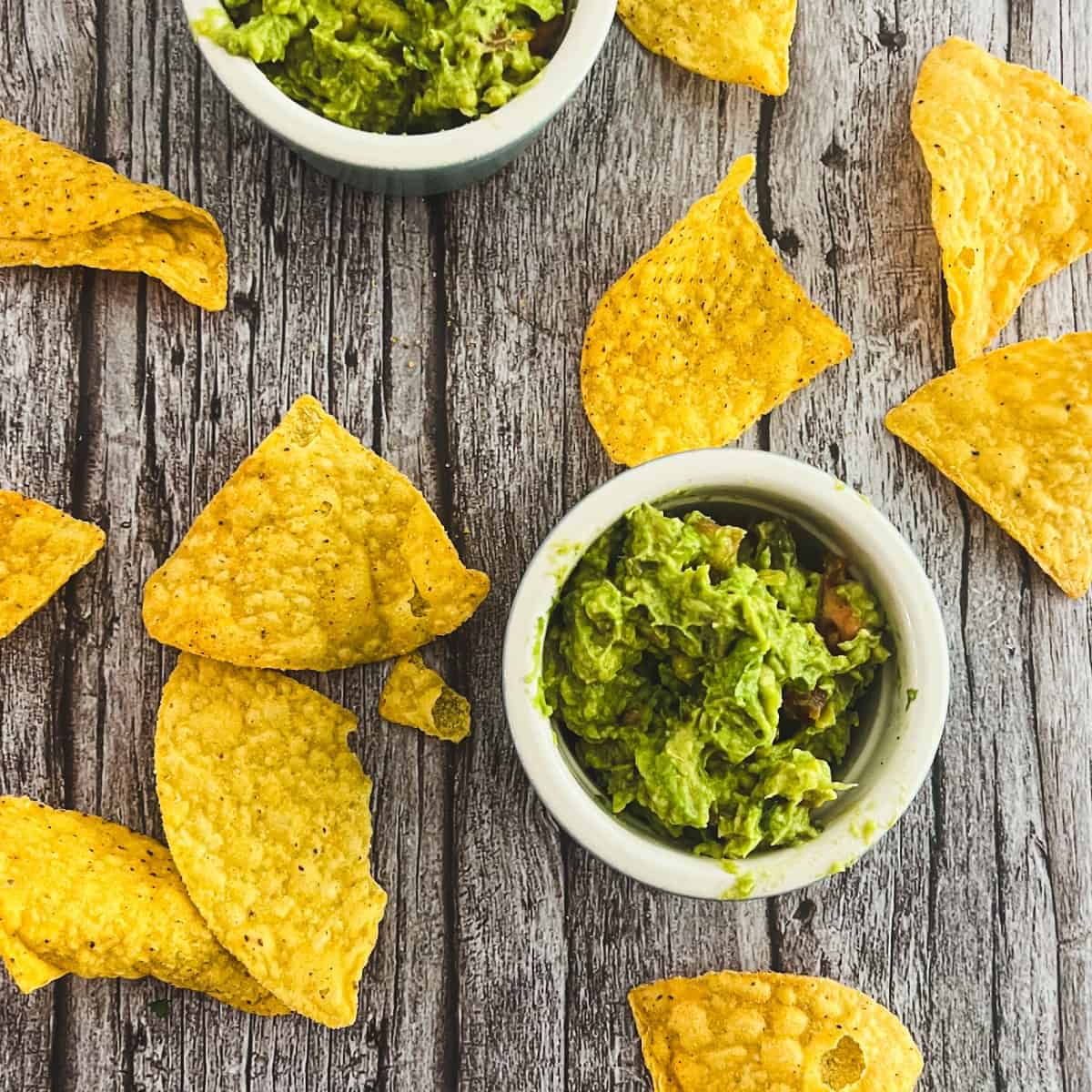 Two bowls of 4-ingredient guacamole recipe with a chunky texture.
Tortilla chips are scattered around the bowls. 