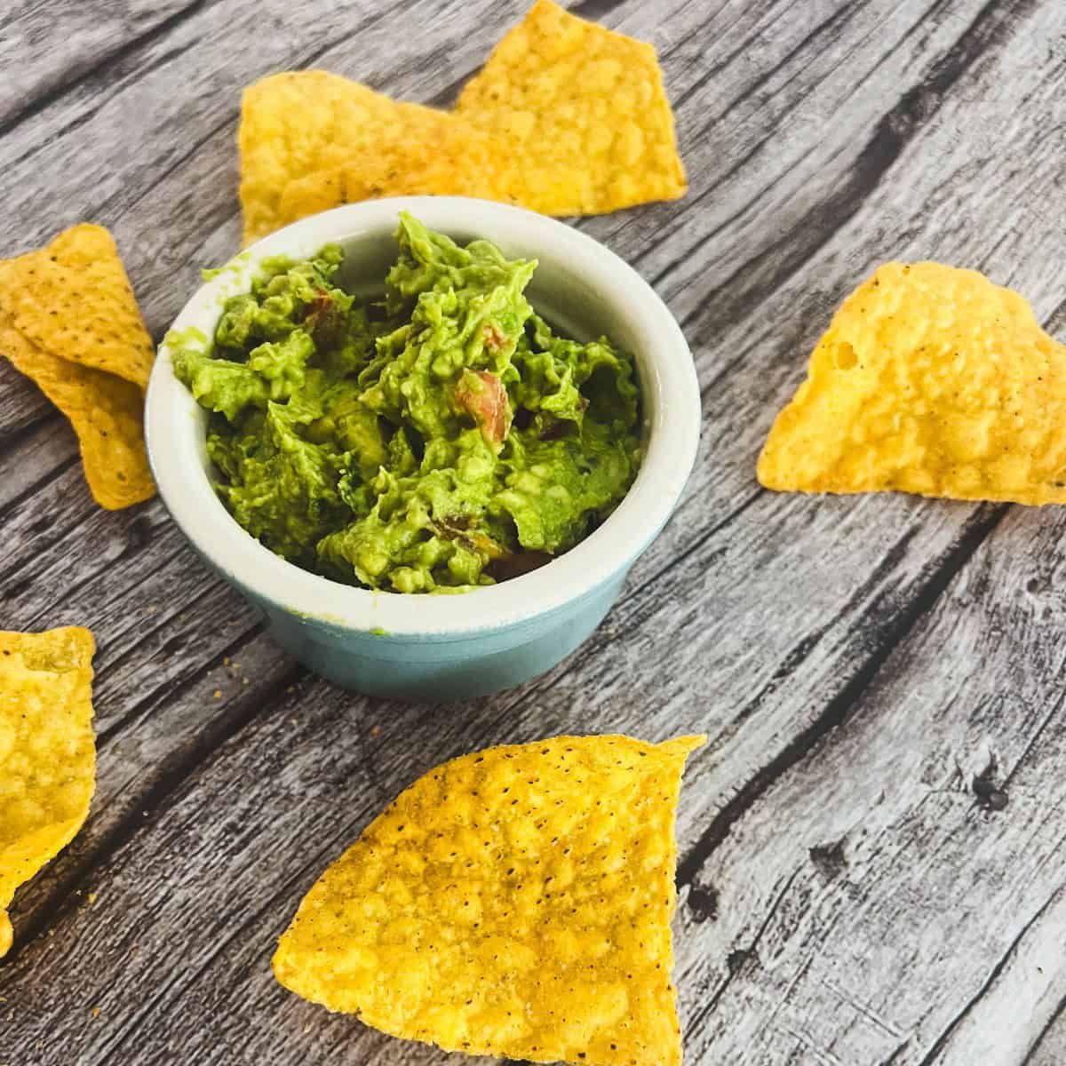 A bowl of 4 ingredients guacamole recipe with a chunky texture, surrounded by tortilla chips.