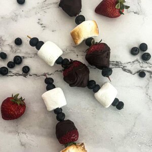 A colorful dessert skewer with fresh strawberries, blueberries, and marshmallows.