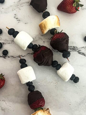 A colorful dessert skewer with fresh strawberries, blueberries, and marshmallows.