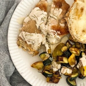 On top of the vegetables are slices of what appear to be light or dark meat chicken. There is a white creamy dijon sauce drizzled over the top of the chicken and vegetables.