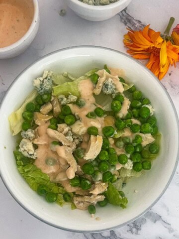 a photo of healthy buffalo chicken salad with chicken, dressing, bleu cheese, peas and celery and lettuce