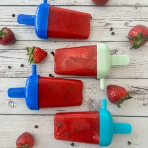 A close-up photo of four red popsicles with visible strawberry chunks. The popsicles are resting on a wooden table and text overlay says how to make strawberry popsicles