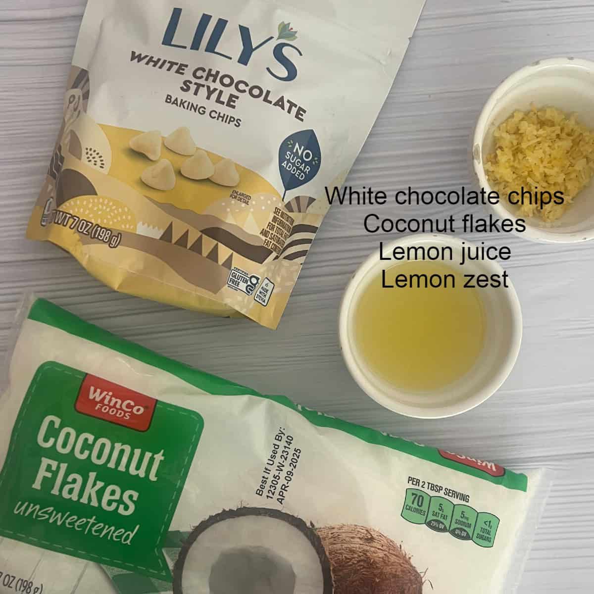 A flat lay image showing the ingredients for lemon coconut bark. From left to right: a bag of Lily's White Chocolate Style Baking Chips, a bag of unsweetened coconut flakes, a small bowl of white chocolate chips, a small bowl of coconut flakes, a small bowl of lemon juice, and a small bowl of lemon zest.