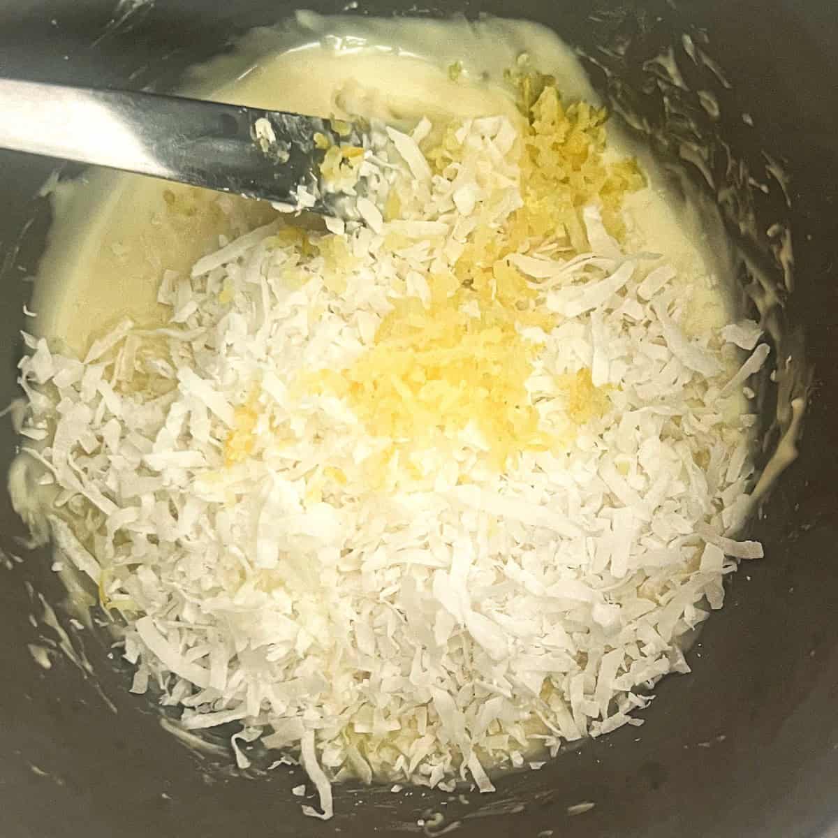 a photo of coconut, lemon juice and lemon zest being stirred into melted white chocolate.