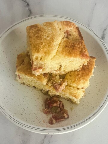 A plate of three squares of rhubarb dump cake mix. The cake is golden brown and has a crumbly texture. A small amount of rhubarb is visible on the plate.